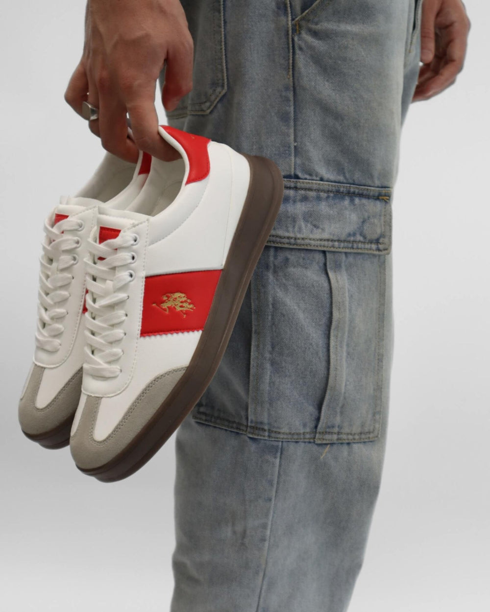 White sneakers with red accents held by a person wearing blue jeans on a white background